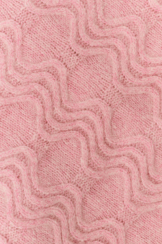 A woman wearing an AFFINA Wave Knit Moxie Cardigan in light pink over a dark green pleated skirt with a pink floral print.