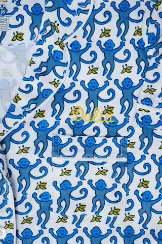 A person with long blonde hair wears Roller Rabbit Monkey Long Sleeve Polo Pajamas in blue and white Pima cotton, standing barefoot on a white background.
