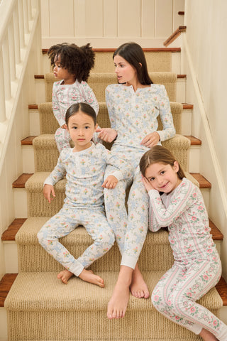 A young girl with long brown hair stands barefoot against a plain background, wearing Roller Rabbit Kids Monkey Block Stripe Pajamas made from soft Pima cotton, featuring playful stripes and monkey motifs.