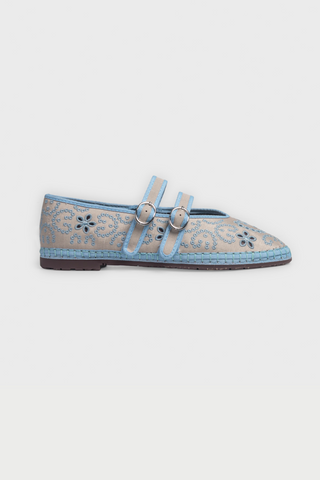 Person holding a pair of gray shoes with decorative elements, wearing a white dress with blue floral patterns.