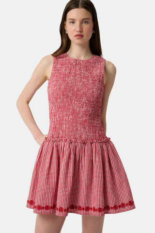 Woman in a red checkered dress standing on a dock with boats in the background