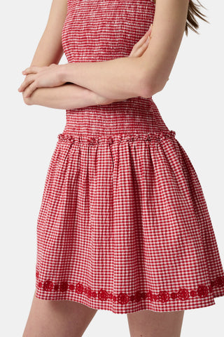 Woman in a red checkered dress standing on a dock with boats in the background
