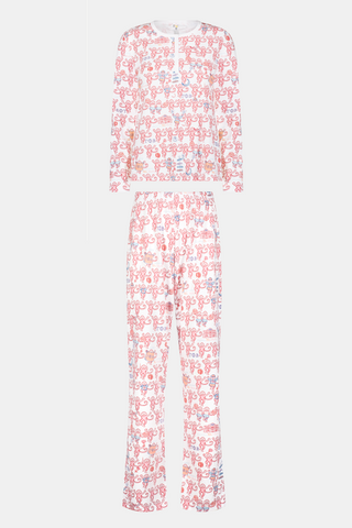 A woman wearing Roller Rabbit Gamma Phi Beta Monkey Pajamas—featuring a white and pink pattern with an elastic waistband—stands outdoors in front of greenery, holding a phone to her ear, a tumbler, and keys. A sweatshirt is tied around her waist, and she wears sunglasses.