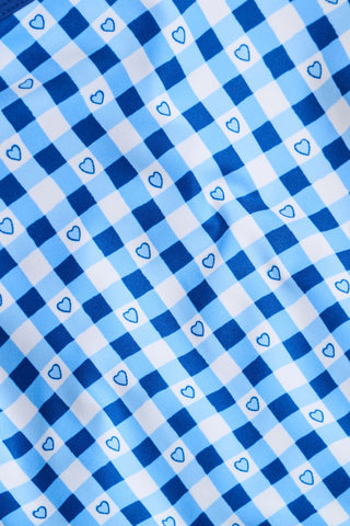 A person wears the Roller Rabbit Gingham Hearts Bella Tank, a blue-and-white checkered racerback style with small heart details. The image is cropped at the shoulders and midsection, showing part of the matching skirt and the person’s head.