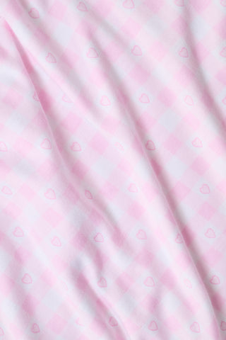 The Gingham Hearts Wyatt Polo Pajamas by Roller Rabbit are a pink and white gingham short-sleeve pajama set, featuring a button-up shirt with chest pocket and matching shorts with a ruffled hem, all crafted from soft Pima cotton. This set is shown on a white background.