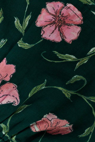 A person wearing a pink cardigan, a dark green Kids Greta Floral Alexis Skirt, and gold ballet flats.