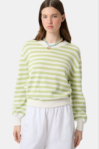 Woman wearing a green and white striped sweater with white pants on a light gray background