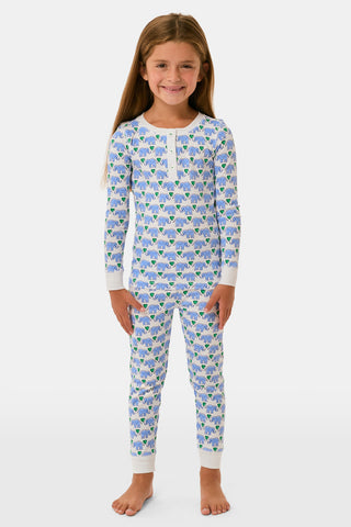 A young girl smiles in Roller Rabbit Kids Hathi Hearts Pajamas with long sleeves and a colorful animal print. She has long brown hair, is barefoot, and stands against a plain white background.