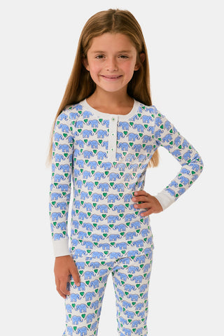 A young girl smiles in Roller Rabbit Kids Hathi Hearts Pajamas with long sleeves and a colorful animal print. She has long brown hair, is barefoot, and stands against a plain white background.