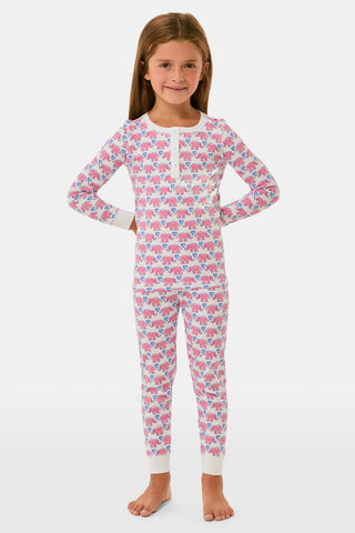 A young girl stands barefoot, smiling with hands on hips, wearing Kids Hathi Hearts Pajamas by Roller Rabbit—soft Pima Cotton pajamas featuring pink and blue elephant patterns on a white background.