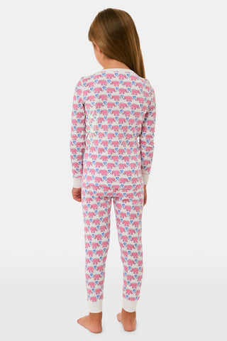 A young girl stands barefoot, smiling with hands on hips, wearing Kids Hathi Hearts Pajamas by Roller Rabbit—soft Pima Cotton pajamas featuring pink and blue elephant patterns on a white background.