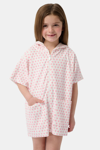 A young girl with straight brown hair smiles in the Roller Rabbit Kids Hearts Jesse Cover Up—a white hooded zip-up with pink heart patterns and two front pockets—standing against a plain light background. Perfect as a cute swim coverup for kids.