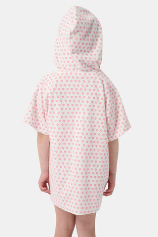 A young girl with long brown hair wears the Roller Rabbit Kids Hearts Jesse Cover Up, a white hooded zip-up towel robe with pink hearts and front pockets, smiling at the camera against a plain light background.