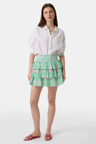 A person models the Roller Rabbit Hydrangea Gingham Siggy Skirt, featuring green and white checks with pink florals, paired with a tucked-in white shirt and red flat sandals. The image displays the skirt from waist to feet.
