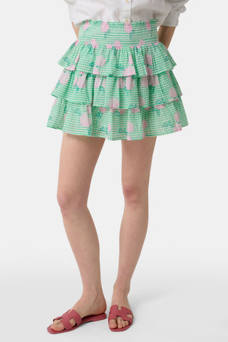 A person models the Roller Rabbit Hydrangea Gingham Siggy Skirt, featuring green and white checks with pink florals, paired with a tucked-in white shirt and red flat sandals. The image displays the skirt from waist to feet.