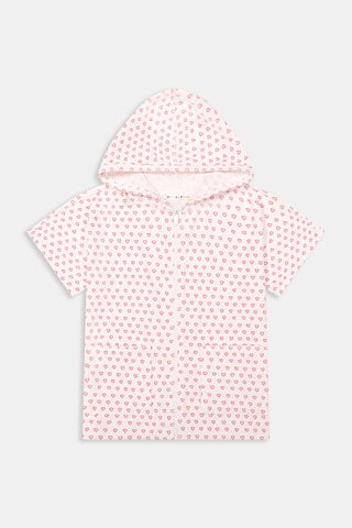 A young girl with straight brown hair smiles in the Roller Rabbit Kids Hearts Jesse Cover Up—a white hooded zip-up with pink heart patterns and two front pockets—standing against a plain light background. Perfect as a cute swim coverup for kids.