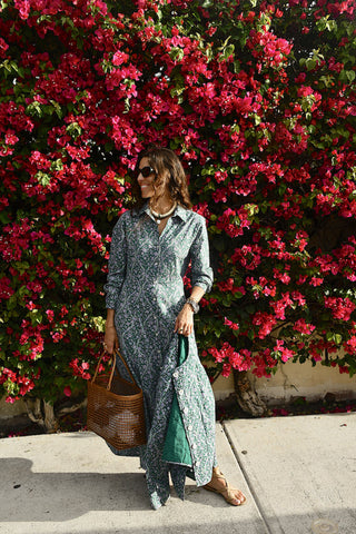 Woman in a long dress standing in front of a vibrant pink flowering bush.