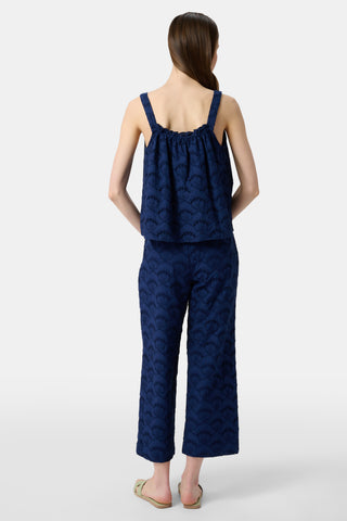 A woman wears the Roller Rabbit Jemina Eyelet Kendall Pant in navy, featuring a scallop pattern, paired with a matching sleeveless top and light green slide sandals. She has long, straight hair.