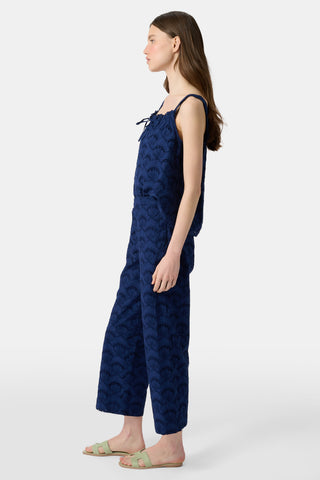 A woman wears the Roller Rabbit Jemina Eyelet Kendall Pant in navy, featuring a scallop pattern, paired with a matching sleeveless top and light green slide sandals. She has long, straight hair.