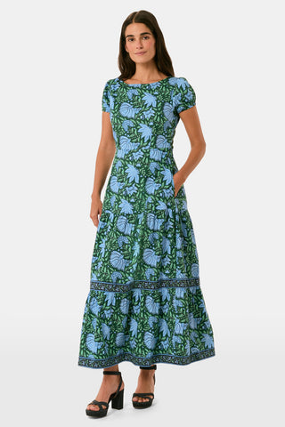 A woman wearing a SAPPHIRE Antonia Floral Jennifer Dress with a green and blue floral print, cap sleeves, tiered midi skirt, and side pockets, paired with black heeled sandals.