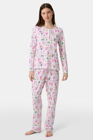 A woman stands barefoot, wearing a matching long-sleeve pajama set with a colorful, playful print on a white background. She faces forward with a relaxed expression, showcasing the cheerful design against a plain white backdrop.