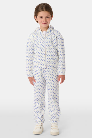 A young girl with curly hair wears the Kids Hearts Harley Hoodie, a cozy blue heart print french terry pajama set, standing against a plain light background with one hand in her pocket.