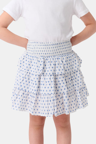 A child wears a white short-sleeved top and the Roller Rabbit Kids Hearts Sami Skirt, featuring three ruffled layers and playful blue heart patterns. The background is plain white.