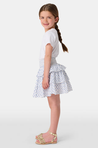 A child wears a white short-sleeved top and the Roller Rabbit Kids Hearts Sami Skirt, featuring three ruffled layers and playful blue heart patterns. The background is plain white.