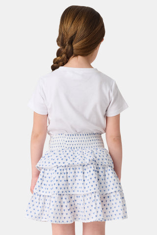 A child wears a white short-sleeved top and the Roller Rabbit Kids Hearts Sami Skirt, featuring three ruffled layers and playful blue heart patterns. The background is plain white.