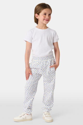 A young child smiles while wearing Roller Rabbit Kids Hearts Sweatpants and a plain white t-shirt, with one hand in the pocket and looking slightly to the side.