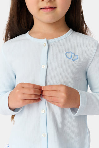 A young girl with long brown hair wears a light blue Roller Rabbit Kids Hearts Pointelle Heidi Cardigan over a white tiered skirt with blue heart patterns, standing and smiling against a plain white background.