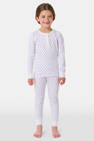 A young child with brown hair smiles barefoot, wearing the Roller Rabbit Kids Hearts Pajamas set with long sleeves and pants against a plain white background.