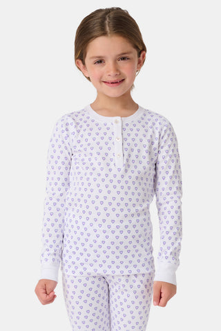 A young child with brown hair smiles barefoot, wearing the Roller Rabbit Kids Hearts Pajamas set with long sleeves and pants against a plain white background.