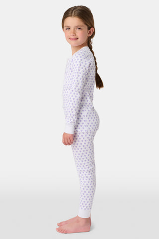 A young child with brown hair smiles barefoot, wearing the Roller Rabbit Kids Hearts Pajamas set with long sleeves and pants against a plain white background.