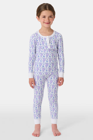 A young child stands smiling in Roller Rabbit Kids Monkey Pajamas, featuring soft Pima cotton, a playful monkey print, white cuffs, and a buttoned neckline, against a plain white background.