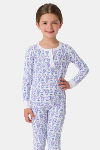 A young child stands smiling in Roller Rabbit Kids Monkey Pajamas, featuring soft Pima cotton, a playful monkey print, white cuffs, and a buttoned neckline, against a plain white background.