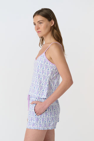 A woman stands barefoot against a plain white background, wearing the Roller Rabbit Monkey Mischa Set—a matching light purple tank top and shorts with a delicate pattern. She has long brown hair and a neutral expression.