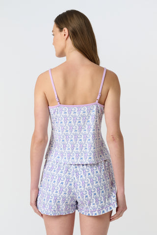 A woman stands barefoot against a plain white background, wearing the Roller Rabbit Monkey Mischa Set—a matching light purple tank top and shorts with a delicate pattern. She has long brown hair and a neutral expression.