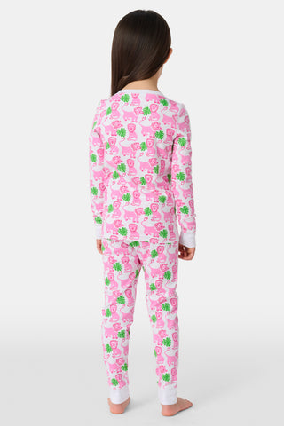 A young girl smiles barefoot against a white background in Roller Rabbit's Kids Leo The Lion Pajamas—soft Pima cotton, long sleeves, white cuffs, and a playful pink-and-green animal print.