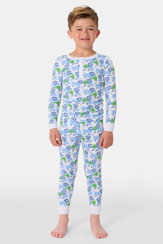 A young child with curly hair smiles barefoot against a plain white background while wearing Kids Leo The Lion Pajamas, crafted from soft Pima cotton.