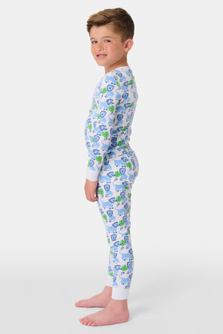 A young child with curly hair smiles barefoot against a plain white background while wearing Kids Leo The Lion Pajamas, crafted from soft Pima cotton.