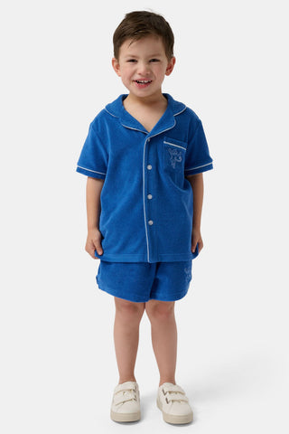 A young child wearing the Roller Rabbit Kids Monkey Embroidery Leo Polo—a navy top with white trim and an embroidered monkey on the chest pocket—smiles with arms raised overhead.