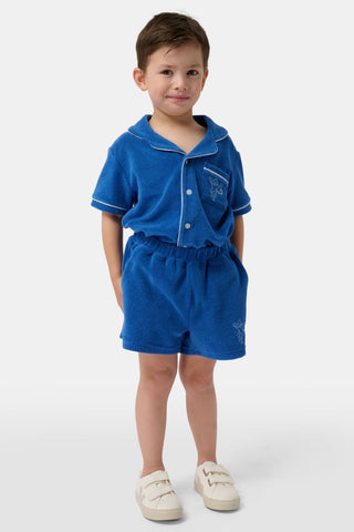 A child wears the Roller Rabbit Kids Monkey Embroidery Hanni Short, navy terry shorts with a monkey embroidered on the left leg, paired with a matching blue top and white velcro sneakers against a plain white background.