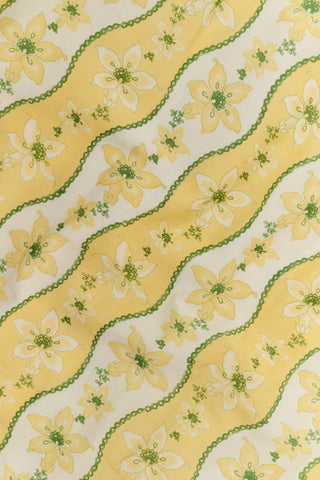 A woman wearing the Roller Rabbit Lillian Floral Stripe Briella Dress, featuring a retro-inspired yellow floral print and puffed sleeves, stands facing the camera and smiles slightly against a plain white background.