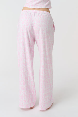 A person stands barefoot on a white background, wearing the Roller Rabbit Lovely Monkey Monroe Pant, light pink loungewear PJ pants with a subtle pattern. The image is cropped above the waist.