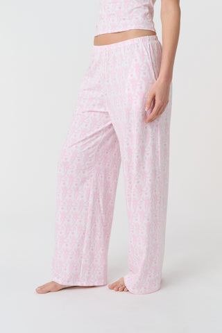 A person stands barefoot on a white background, wearing the Roller Rabbit Lovely Monkey Monroe Pant, light pink loungewear PJ pants with a subtle pattern. The image is cropped above the waist.