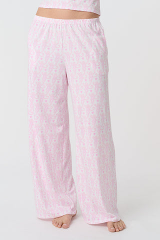 A person stands barefoot on a white background, wearing the Roller Rabbit Lovely Monkey Monroe Pant, light pink loungewear PJ pants with a subtle pattern. The image is cropped above the waist.