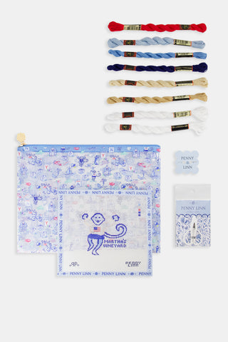 The PENNY LINN Monkey On The Vineyard Kit includes colorful threads, a zippered blue project bag, a small white canvas with a blue dog marked “Martha’s Vineyard,” two thread holders, and a needle in packaging.