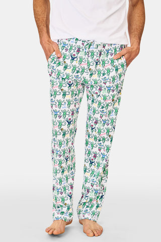 A man stands barefoot against a white background, wearing Mens Boston Monkey Simon Pant—white Pima Cotton pajama pants with a colorful cartoon flower and plant print—paired with a plain white T-shirt.
