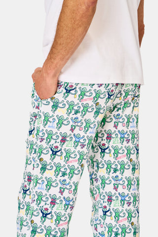 A person wearing Mens Boston Monkey Simon Pant—white Pima cotton pants with a colorful monkey pattern—stands hand-in-pocket, shown waist-down with a plain white shirt; ideal for cozy pajama wear in Boston.